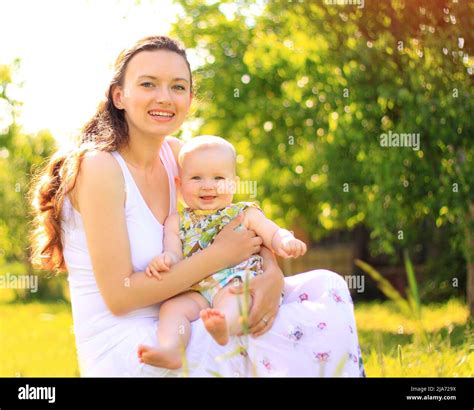 Mother gently holding her baby on a grassy lawn, sunlight filtering through trees